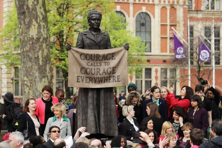 Millicent Fawcett statue holding a sign that says: 'Courage calls to courage everywhere' surrounded by a crow of women. 